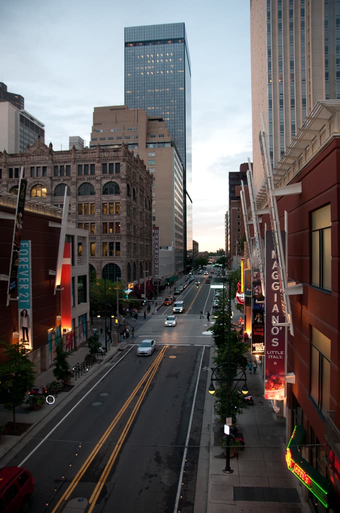 Eine Stadtszene mit einer StraÃe voller Autos unten, flankiert von GebÃ¤uden und Wolkenkratzern auf beiden Seiten, unter einem Himmel oben.