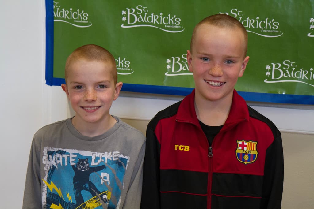 Zwei Jungen nebeneinanderstehend, die lächeln, mit einem Banner im Hintergrund mit Text.