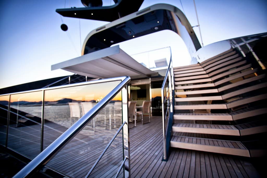 Ein modernes Glasgebäude mit Treppen auf der rechten Seite, Stühle um einen Tisch auf der linken Seite und eine Glasabsperrung links unten.