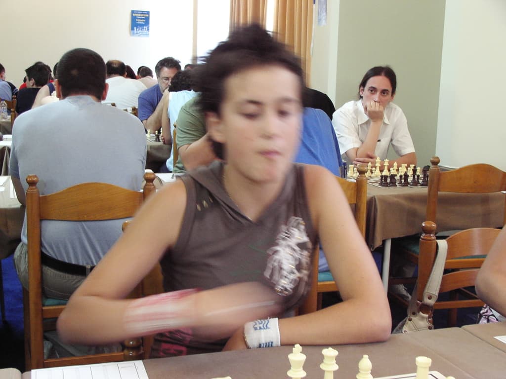 Ein Raum mit Menschen an Tischen beim Schachspielen, mit einer Vorhangwand und einem Foto in der Ecke.