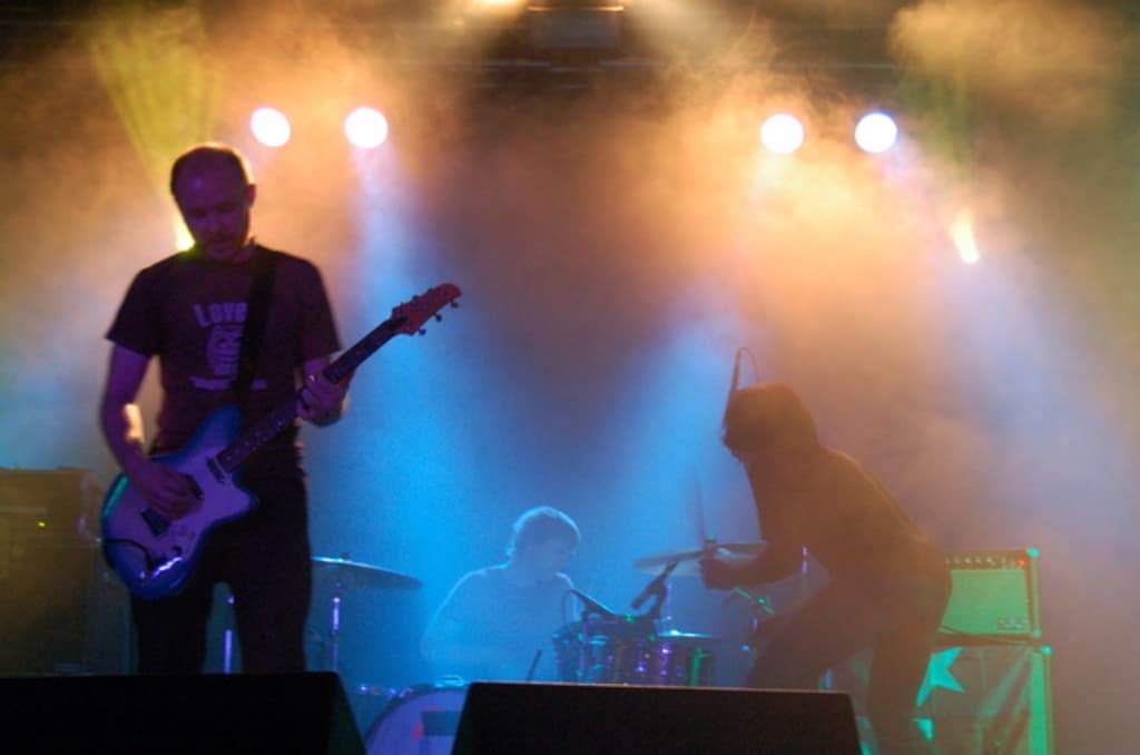 Ein musikalisches Konzert mit Lichtern oben, Musikern in der Mitte und Lautsprechern auf der linken und rechten Seite.