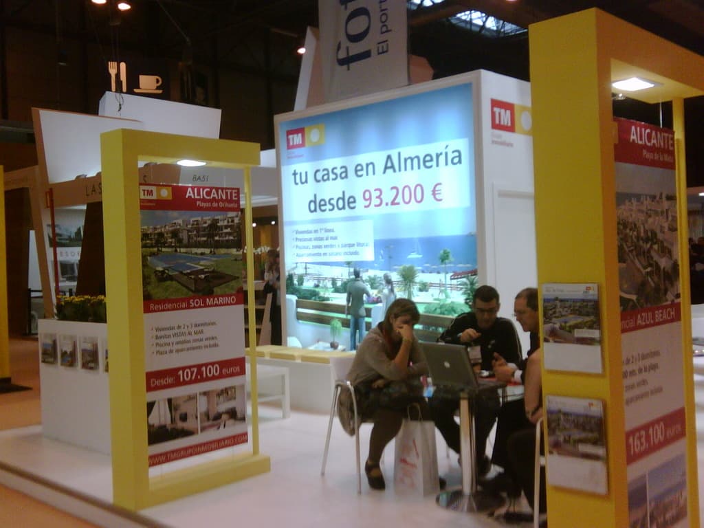 Eine Gruppe von Menschen, die um einen Tisch sitzen und auf einen Laptop schauen, mit mehreren Flyern, die verschiedene Werbeanzeigen neben ihnen anzeigen.