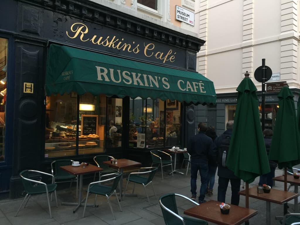 Eine Gruppe von Menschen vor einem Cafe mit der Aufschrift "Ruskins Cafe".