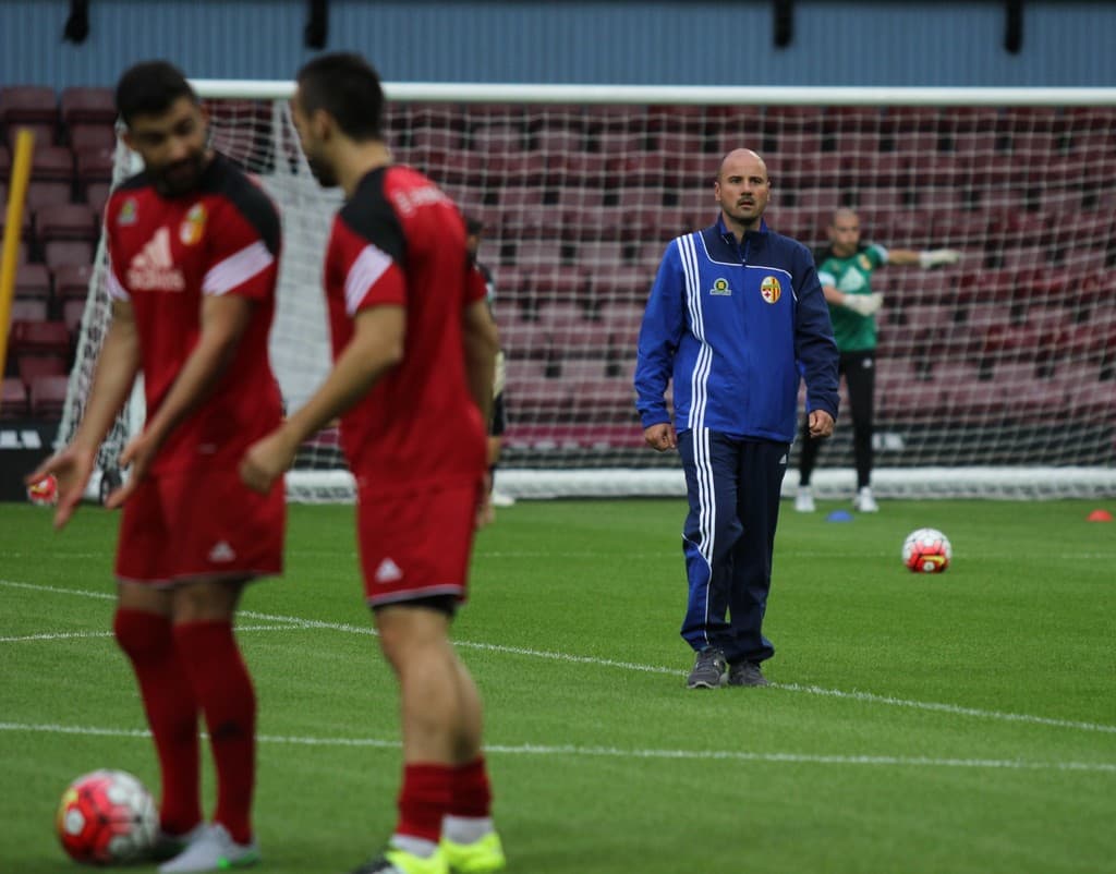 Ein Fußballfeld mit darauf stehenden Spielern, zwei Bällen und einem leeren Stadion im Hintergrund.