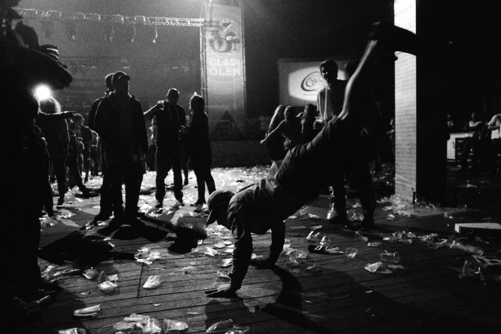 Eine Person führt eine Stunt-Show in der Mitte durch, während Zuschauer im Hintergrund stehen und Plastikteile auf dem Boden verstreut sind und ein Schild mit Text und Lichtern oben zu sehen ist.