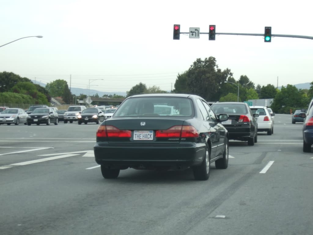 Eine vielbefahrene Stra├če mit mehreren Fahrzeugen, drei Strommasten und einem Verkehrszeichen auf der rechten Seite unter einem klaren Himmel.