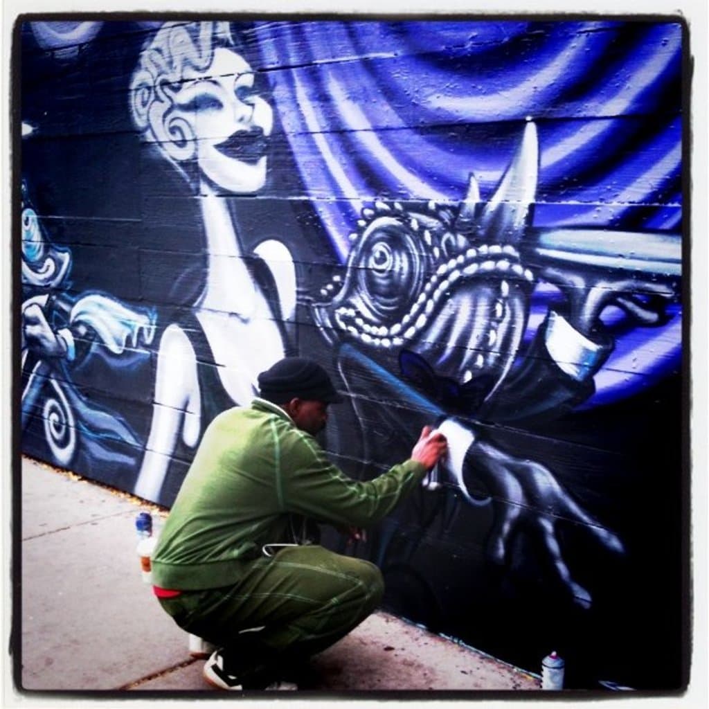 Eine Person hält eine Flasche, während sie auf einer Straße mit mehreren anderen Flaschen drumherum steht, mit einer Graffiti-bedeckten Wand im Hintergrund.