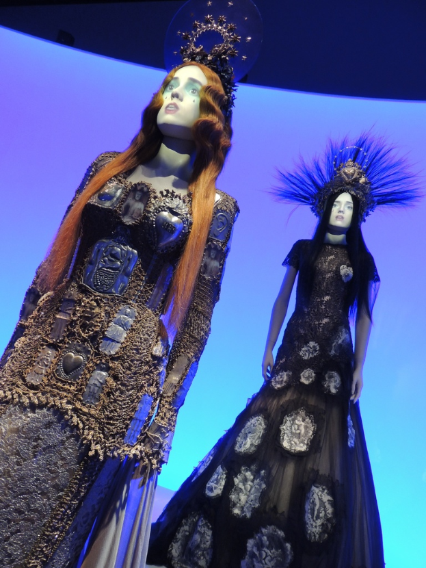 Zwei Schaufensterpuppen mit unterschiedlichen Kleidern und Kopfbedeckungen in einem Geschäft.