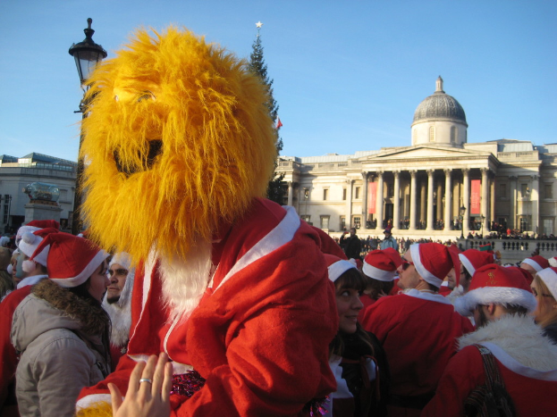 Eine Person in einem Santa-Kostüm mit Tiger-Maske steht mit anderen in Santa-Kostümen vor einem Gebäude.