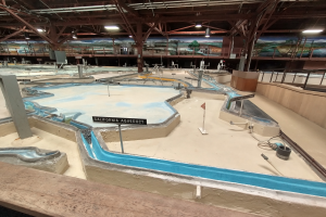 Ein großes Indoor-Wasserpark mit zahlreichen Wasserrutschen, Pfählen, Texttafeln, Deckenleuchten und Wandgemälden, das wie ein Minigolfplatz gestaltet ist.