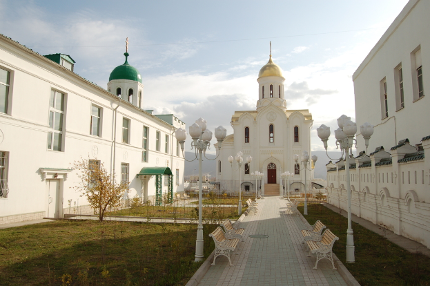 Eine Stadtansicht mit Gebäuden mit sichtbaren Fenstern, einer grünen Fläche mit einem Lichtmast, Blumenkasten, Bänken und einem Fußweg unter einem bewölkten Himmel.