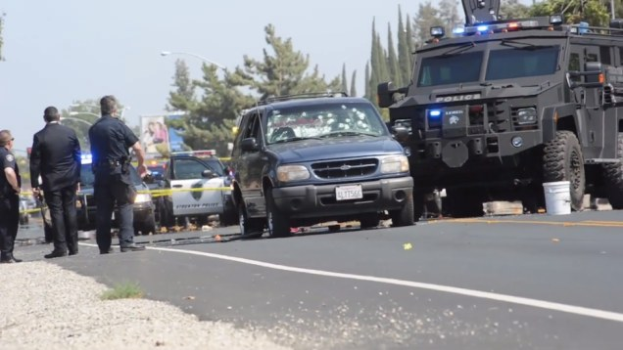 Polizeiauto und Lkw neben einer Gruppe von Menschen, einem Eimer, Steinen, einer Schleife, einem Banner, einem Straßenschild, Bäumen und einem bewölkten Himmel in Fresno, Kalifornien.