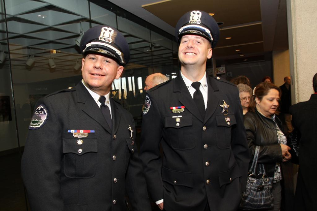 Zwei lächelnde Beamte im Vordergrund, mit Menschen in der Mitte, Glasfenstern links, Lampen und Decke oben und Säulen und Menschen rechts.