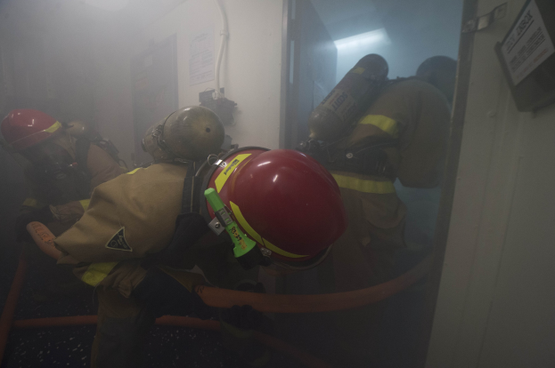Feuerwehrleute in Schutzausrüstung betreten einen raucherfüllten Raum mit Sauerstoffflaschen und Rohren.