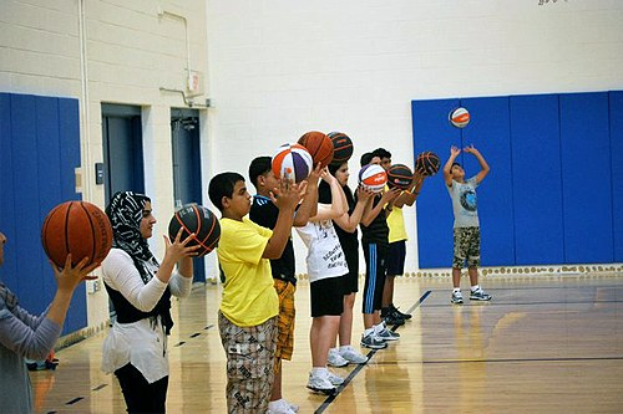 Junge Menschen mit Basketballs auf einem Basketballfeld mit Türen und einer Wand im Hintergrund.