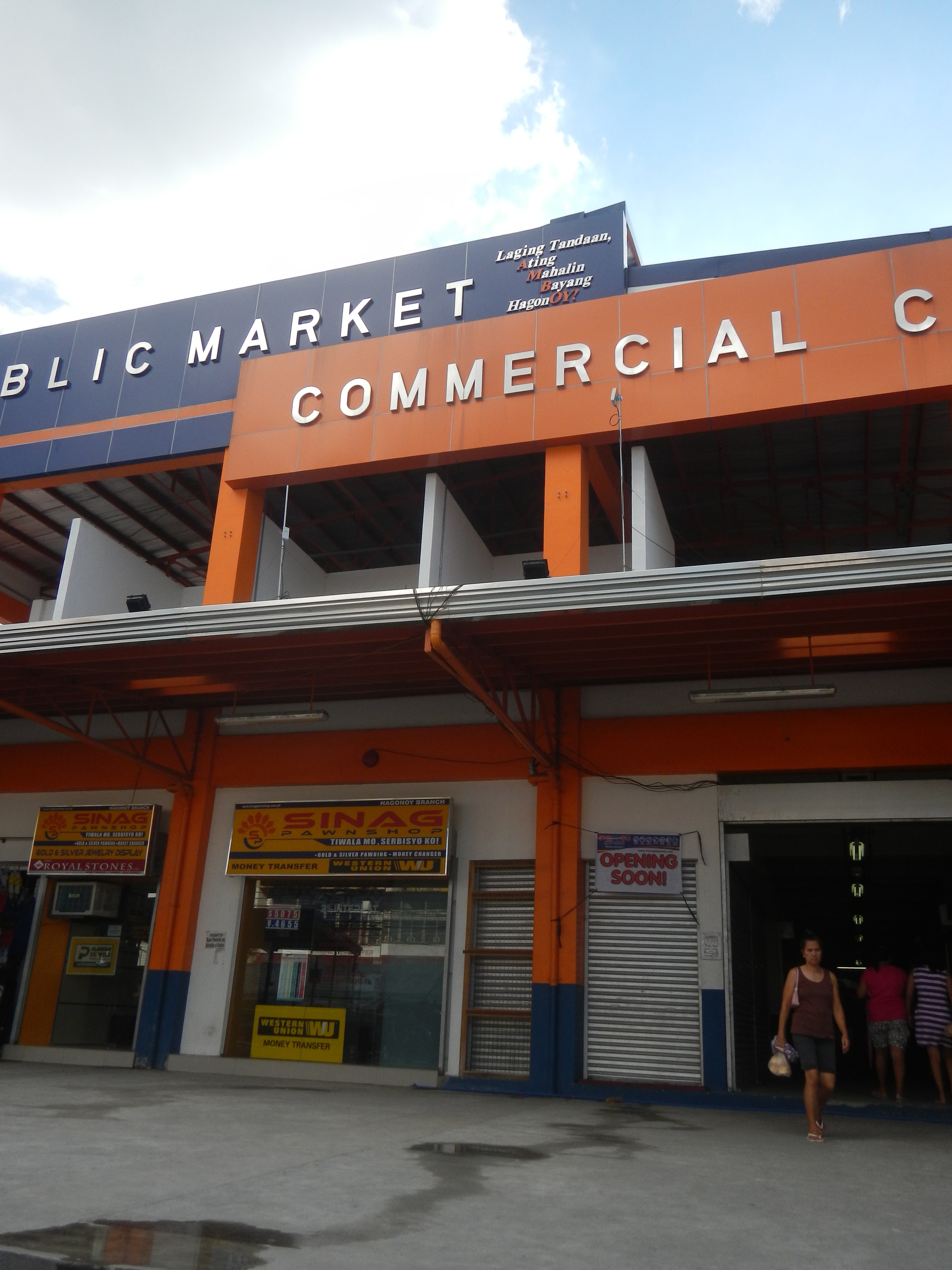 Ein öffentliches Marktzentrum mit Menschen davor, Text auf dem Gebäude und sichtbarer Himmel oben.