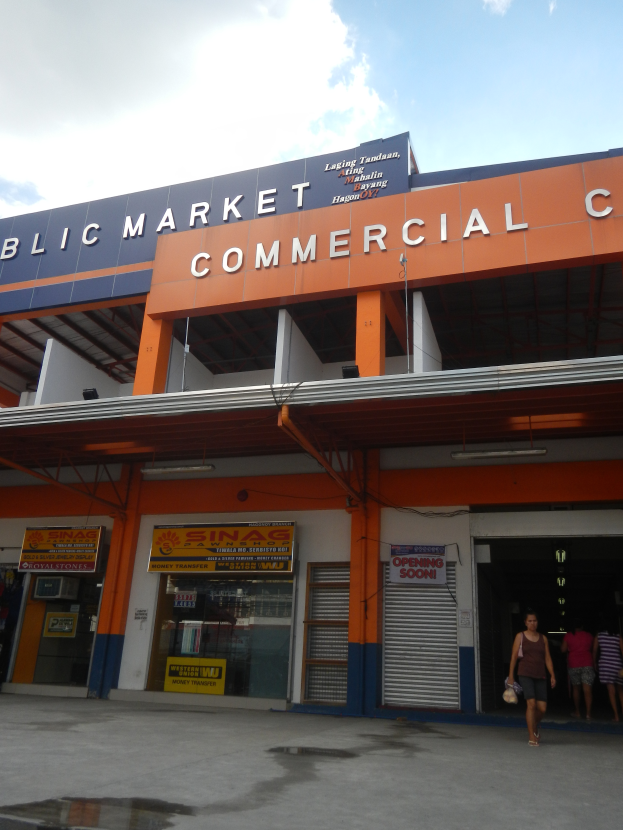 Ein öffentliches Marktzentrum mit Menschen davor, Text auf dem Gebäude und sichtbarer Himmel oben.