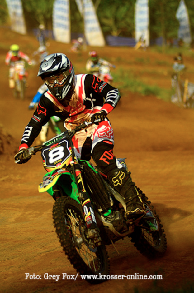 Mehrere Motorradfahrer mit Helmen auf der Rennstrecke, mit Text am unteren Bildrand.