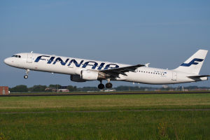 Ein Airbus A320-200 der Finnair, der von Frankfurt Airport abhebt, mit Gras darunter, Gebäuden und Bäumen im Hintergrund und einem klaren blauen Himmel darüber.