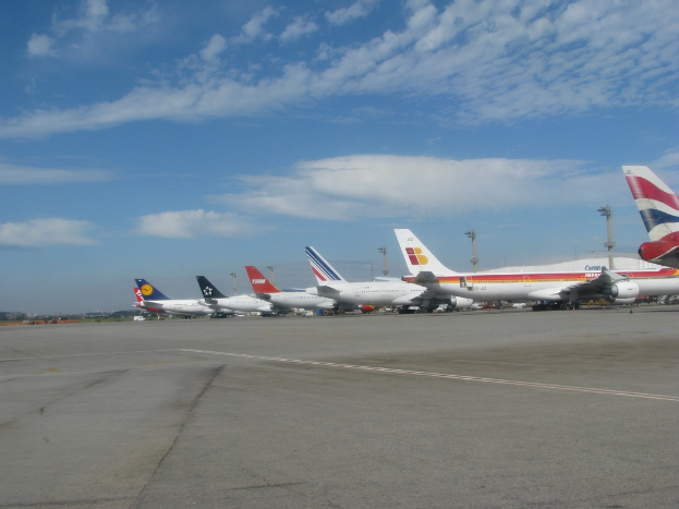 Eine Start- und Landebahn mit einigen Flugzeugen, Pfählen, Kabeln und Wolken am Himmel.