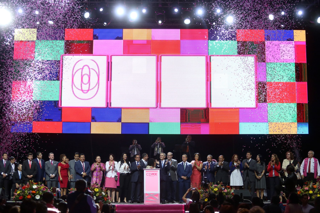 Gruppe von Menschen auf einer Bühne mit einem Podium, Blumengestecke auf beiden Seiten, Menschen mit Kameras und ein großer Bildschirm mit Lichtern im Hintergrund für die Eröffnungszeremonie des 2018 China International Film Festival.