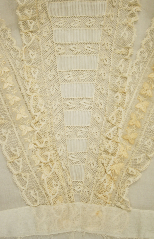 Nahaufnahme eines weißen Kleides mit zarter, detailreicher Spitzenverzierung in verschiedenen Mustern und Formen, entworfen für einen leichten, luftigen Sommertag.