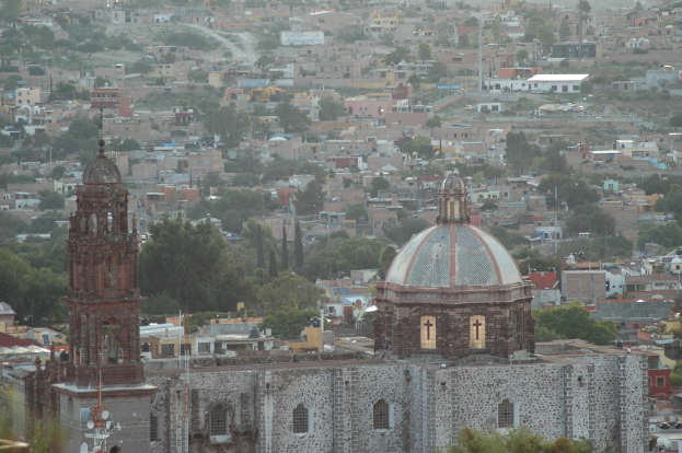 Eine Luftaufnahme einer Stadt mit BÃ¤umen, GebÃ¤uden, StraÃen, MÃ¤sten und einer Kirche im Vordergrund.