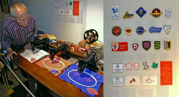 Ein Mann mit Brille steht hinter einem Tisch mit einer Platte, die Abzeichen, Nähmaschinen, Kleidung und verschiedene farbige Fäden zeigt.