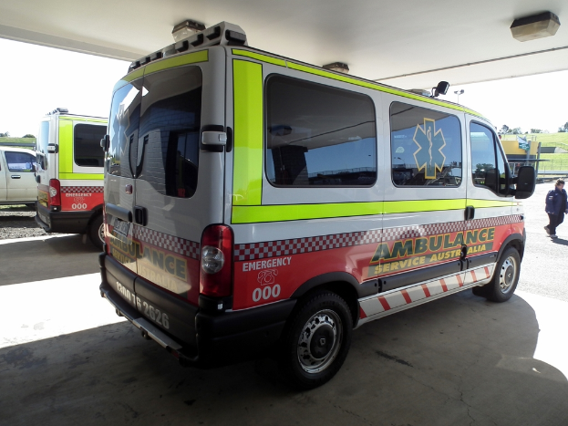 Zwei Krankenwagen nebeneinander unter einem Dach geparkt, mit einer Person rechts und einem Mann neben dem linken Krankenwagen.