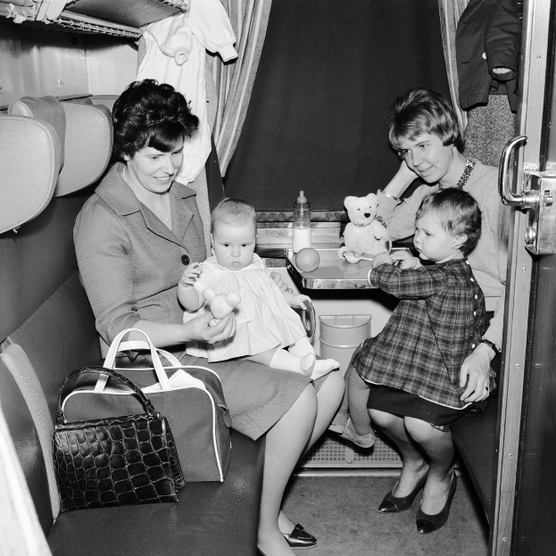 Ein Schwarz-Weiß-Foto von zwei Frauen und zwei Kindern, die in einem Zug sitzen, wobei eine Frau ein Baby hält und die andere zwei Kinder hält.