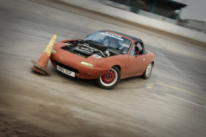 Eine Person fährt ein rotes Auto auf einer Rennstrecke, überholt einen Verkehrskegel, mit einem unscharfen Hintergrund, der hohe Geschwindigkeit andeutet.