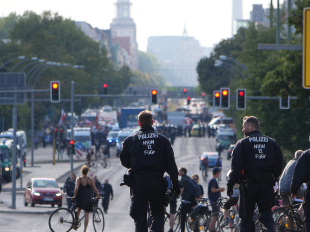 Polizeibeamte fahren mit Fahrrädern eine straße entlang, gesäumt von Bäumen und einem klaren blauen Himmel.