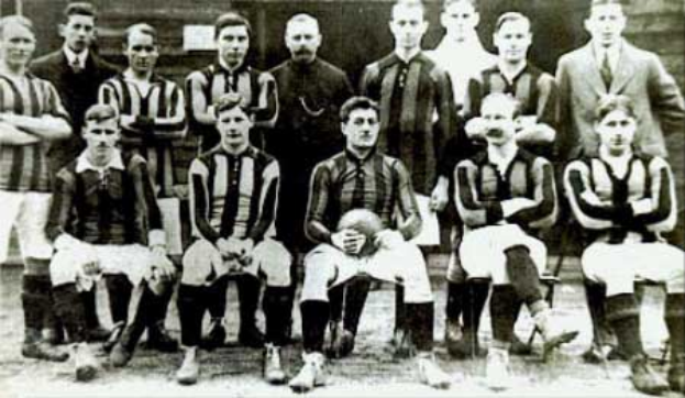 Ein Schwarz-Weiß-Foto einer Fußballmannschaft, einige stehen, einige sitzen, vor einer Wand, mit dem Text 'Ballymena Football Club' unten.