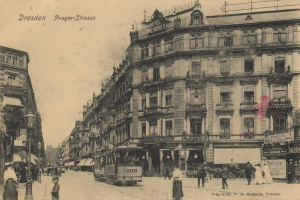 Ein Schwarz-Weiß-Foto einer Straßenstraße in Dresden, Deutschland, das Menschen, Fahrzeuge, Gebäude und einen bewölkten Himmel zeigt.