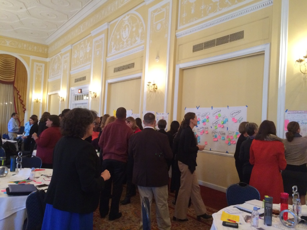 Eine Gruppe von Menschen, die Plakate und Schaubilder an einer Wand in einem Kunstmuseum betrachtet.