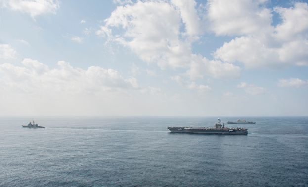 Three ships are sailing on a body of water under a cloudy sky.