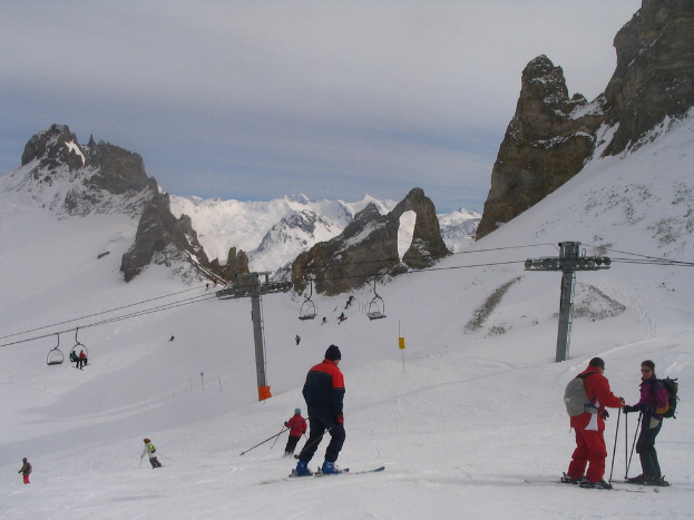 Menschen in Pullovern Ski auf Eis mit einer Seilbahn, Bergen und einem bewölkten Himmel im Hintergrund.