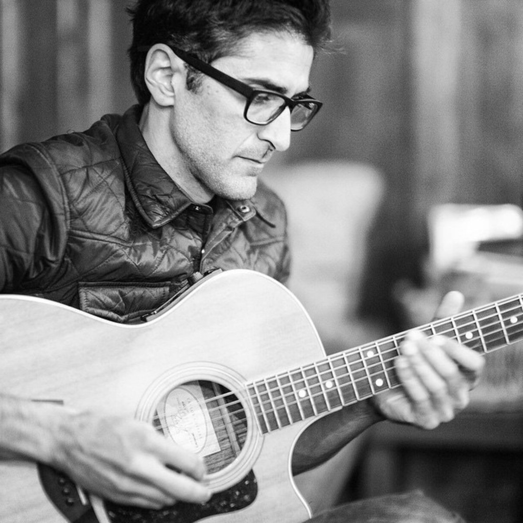 Ein Mann in einer Jacke, der eine Gitarre spielt.