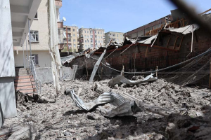 Die Auswirkungen eines israelischen Luftangriffs in Gaza-Stadt, der ein zerstörtes Gebäude mit Schutt, eingestürzten Wänden, Metallstangen, einem Zaun, einer Treppe, nahen Gebäuden mit Fenstern, einigen Bäumen und einem bewölkten Himmel zeigt.