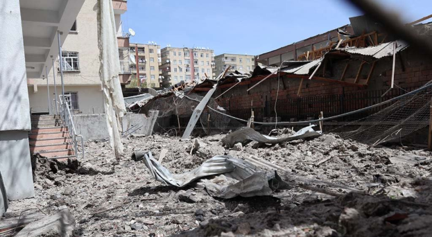 Die Auswirkungen eines israelischen Luftangriffs in Gaza-Stadt, der ein zerstörtes Gebäude mit Schutt, eingestürzten Wänden, Metallstangen, einem Zaun, einer Treppe, nahen Gebäuden mit Fenstern, einigen Bäumen und einem bewölkten Himmel zeigt.