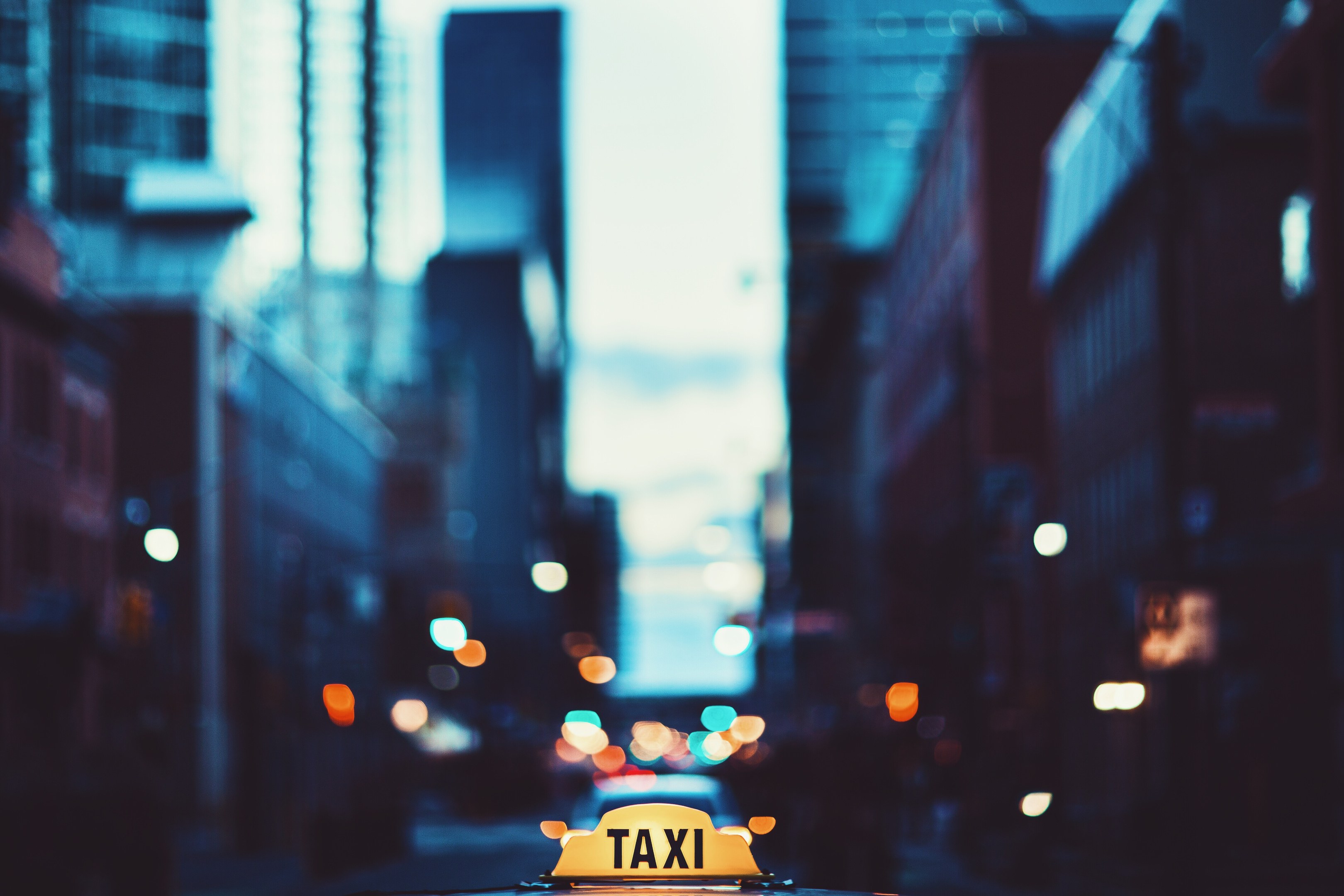 Ein gelbes Taxi, das nachts eine Stadtstraße entlangfährt, flankiert von Gebäuden mit einem unscharfen Hintergrund.