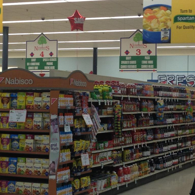 Ein Supermarkt-Innenraum mit sichtbaren Lebensmitteln, Deckenlampen und Schildern.