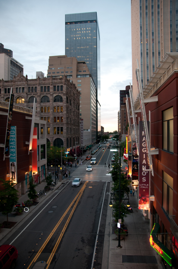Eine Stadtszene mit einer StraÃe voller Autos unten, flankiert von GebÃ¤uden und Wolkenkratzern auf beiden Seiten, unter einem Himmel oben.