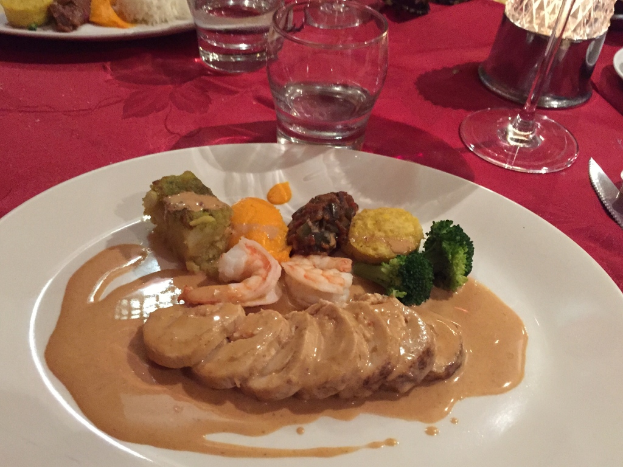 Ein Tisch mit roter Decke, gedeckt mit Tellern, Gläsern, einem Messer, einer Lampe, einem Getränk und verschiedenen Speisen.