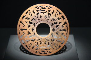 Ein chinesischer geschnitzter Jade-Teller in einem Museum ausgestellt, mit detaillierten Oberflächen-Schnitzereien und einem dunklen Hintergrund.