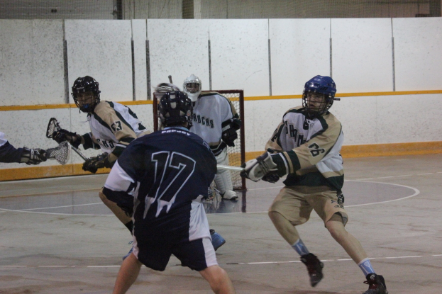 Personen in Helmen mit Stöcken scheinen in einem Innenraum zu kämpfen, mit einem Netz im Hintergrund.