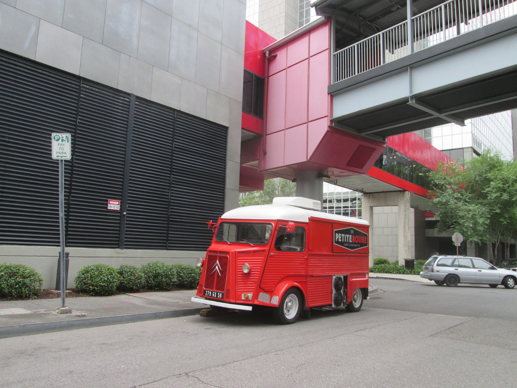 Ein Van steht in der Mitte des Bildes mit einem Auto auf der rechten Seite, im Hintergrund sind Gebäude zu sehen.