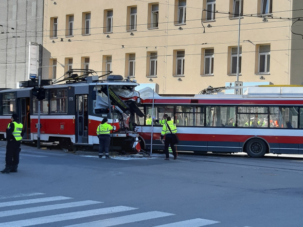Eine rote und weiße Straßenbahn, die an der Seite der Straße in einen Unfall verwickelt ist, mit ein paar Menschen in der Nähe und einem Gebäude im Hintergrund.