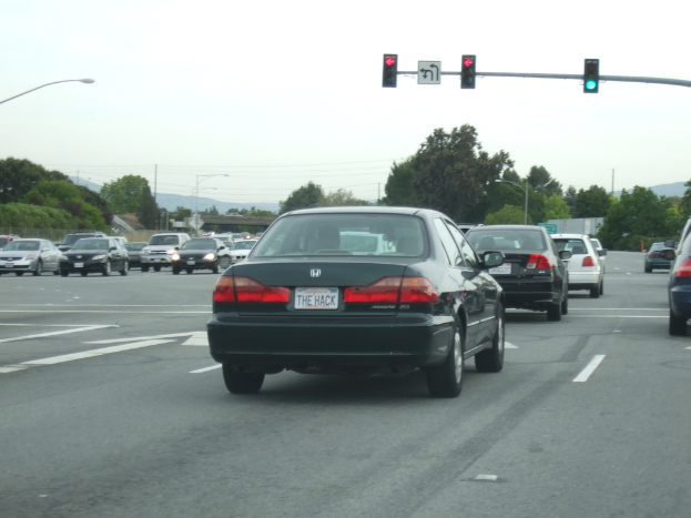 Eine belebte Straße mit zahlreichen Fahrzeugen, drei Strommasten und einem Verkehrssignal auf der rechten Seite unter einem klaren Himmel.