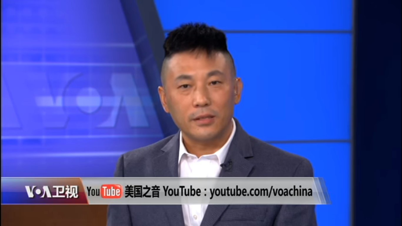 Ein chinesischer Nachrichtensprecher im Anzug und Krawatte erscheint auf einem Fernseher mit Text unten und einem blauen Hintergrund.